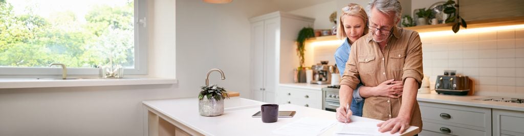 Man and woman standing together in kitchen writing documents